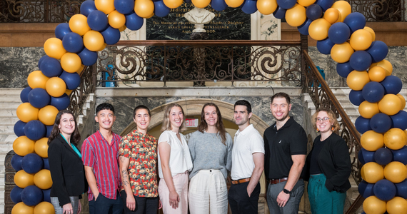 2023 Doctoral Fellows in front of a blue and gold balloon arch in Main Building